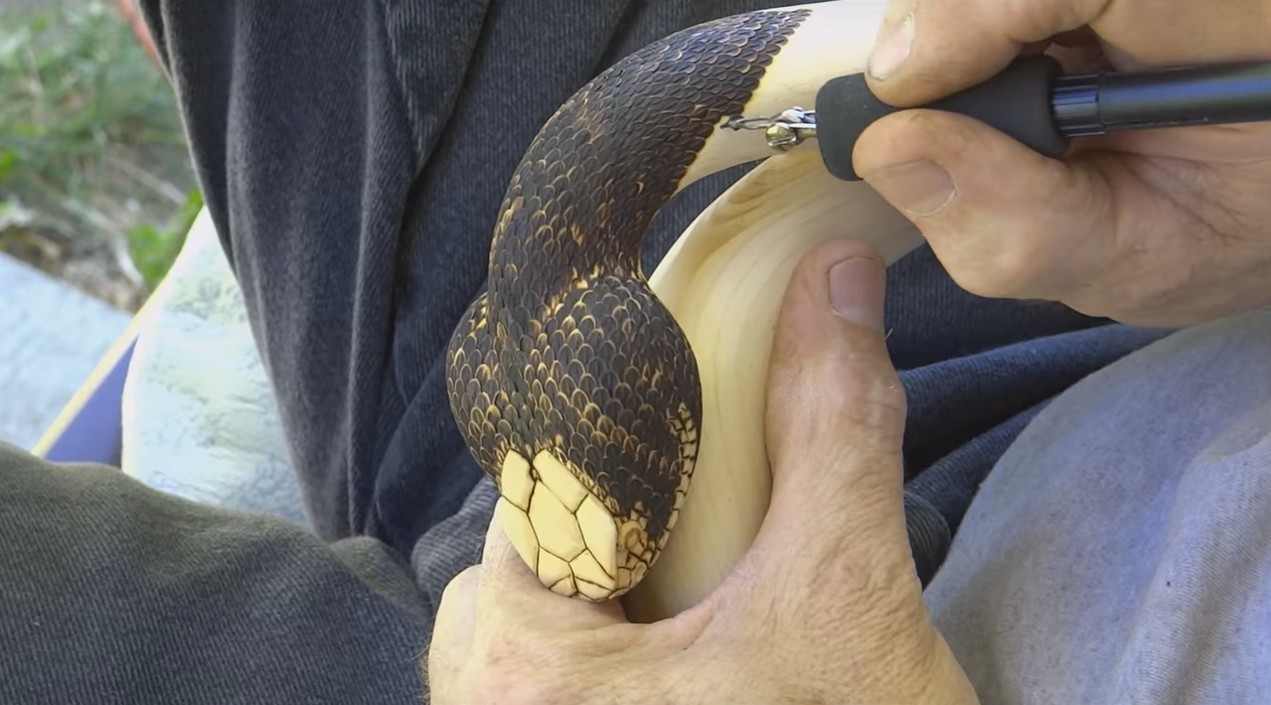 Столяр с прямыми руками вырезает деревянную трость со змеей